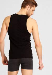 Schwarzes ärmelloses Tanktop aus weichem Stoff, mit einem runden Ausschnitt und einer engen Passform, kombiniert mit dunkelgrauen Shorts.
