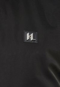 Μαύρο ύφασμα με ένα μικρό τετράγωνο έμπλαστρο που διαθέτει ασημί μεταλλικό λογότυπο και κείμενο "Karl Lagerfeld" στο κέντρο.