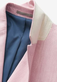 Helles rosa Blazer mit cremefarbenem Kragen und dunkelblauer Innenauskleidung, im Close-up auf weißem Hintergrund dargestellt.
