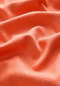 Korallenfarbener Stoff mit leichtem, strukturiertem Erscheinungsbild, der weiche, sanfte Falten und ein gleichmäßiges Webmuster zeigt.