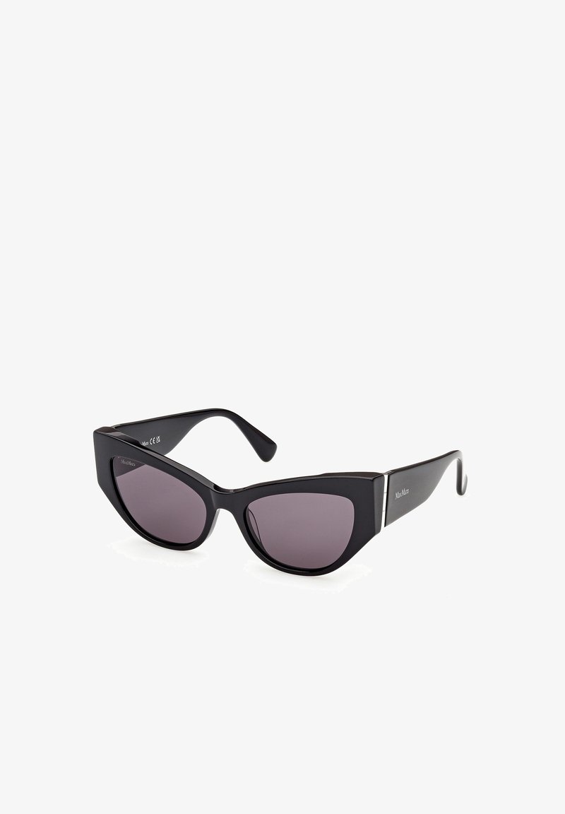 Lunettes de soleil papillon noires avec des verres teintés foncés et des montures épaisses et brillantes, inclinées sur un fond blanc.