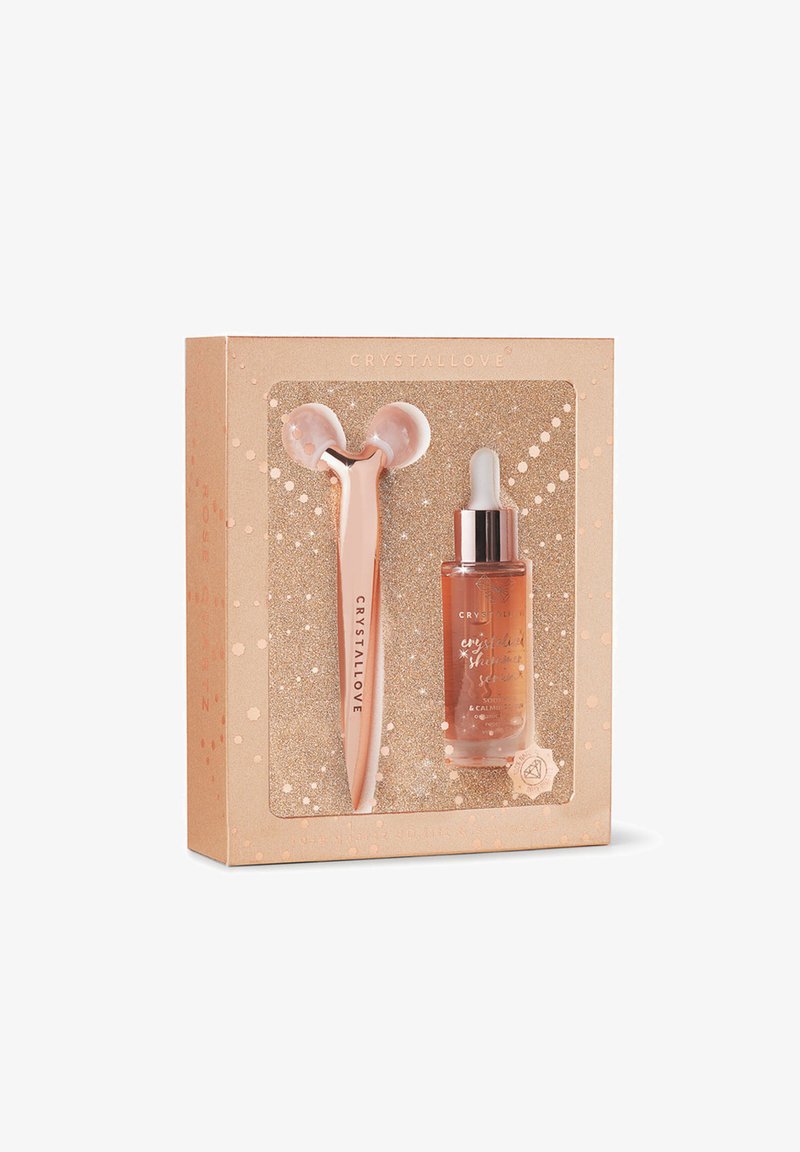 Różowo-złoty wałek do masażu twarzy i serum w ozdobnym pudełku z dodatkiem brokatu, z zaokrąglonymi kształtami i szklaną teksturą.