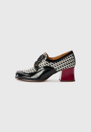Scarpa in vernice nera con un motivo geometrico bianco, punta tonda, design con lacci e tacco a blocco bordeaux in contrasto.