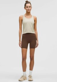 Svetlo olivová tielko s textúrovaným povrchom, v kombinácii s hnedými šortkami s vysokým pásom. Outfit dopĺňajú béžové športové topánky a biele ponožky.