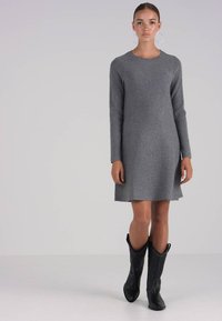 Pelēks adīts kleitas modelis ar garām piedurknēm, nedaudz izplešotas apakšdaļas, izgatavots no mīksta materiāla. Apvienots ar melniem dekoratīviem kovboju zābakiem.