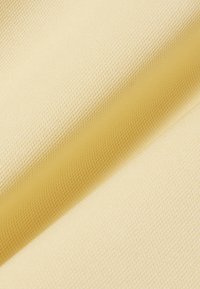 Gros plan sur un tissu texturé jaune clair avec un motif de petits points en relief et des plis visibles créant de douces ombres.