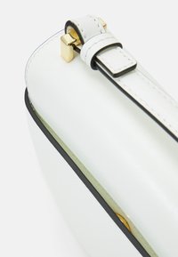 Biała skórzana torebka z czarnym wykończeniem, z złotym prostokątnym detalem i gładką fakturą. Kompaktowy, prostokątny design.