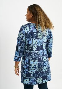 Mehrfarbige Tunika mit einem Patchwork-Design in Blau-, Grün- und Marineblau-Quadraten. Hergestellt aus weichem Stoff mit Dreiviertelärmeln.