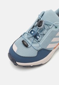 Scarpa sportiva azzurra chiara con tomaia in mesh, dettagli blu navy e un sistema di allacciatura rapida. Presenta una suola texturizzata e dettagli con il marchio sul lato.