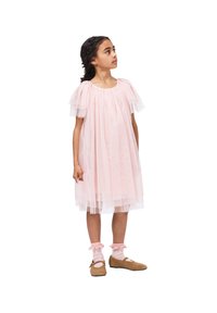 Robe en tulle rose clair avec des manches courtes bouffantes superposées, longueur au genou, portée avec des chaussettes crème et des chaussures plates marron. Détails minimaux.
