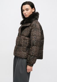 Jopič v bež barvi z črnim leopardjim potiskom, z mehkim temnim krznenim ovratnikom, širokim krojem in rebrastimi manšetami. Mehka tekstura s prešitim vzorcem.