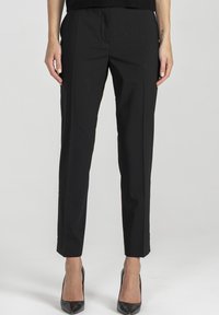 Czarne, dopasowane spodnie o wąskim kroju, gładka tkanina, subtelne detale zakładek, długość 7/8 oraz kieszenie z przodu bez fałd. W połączeniu z czarnymi szpilkami.