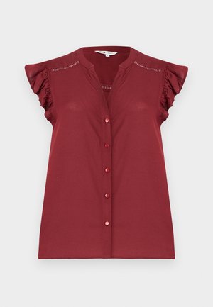 Nööbiga varrukateta burgundia värvi pluus volangsete varrukapealsete ja õlgade lähedal silmadega detailidega.