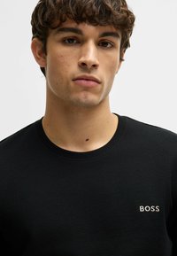Čierny sveter z waffle pleteniny s okrúhlym výstrihom a jemným logom "BOSS" v bielej farbe na ľavej hrudi. Mäkka textúra, voľný strih.