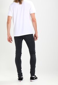 Vaqueros skinny negros con un diseño clásico de cinco bolsillos, material de mezclilla suave y una textura lisa; combinados con una camiseta blanca y zapatillas.