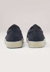 Sneaker in suede blu navy con un design a profilo basso, tomaia testurizzata e suole in gomma crema a contrasto. Posteriore arrotondato con dettaglio del pull tab.