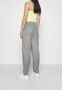 Graue, leichtgewichtige Jogginghosen mit elastischem Bund, lockerem Schnitt und Bündchen an den Knöcheln. Kombiniert mit einem leuchtend gelben Tanktop.