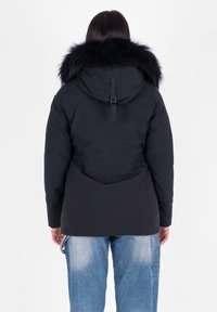 Zwarte pufferjack met een met bont gevoerde capuchon. Beschikt over een getailleerde taille en grote zakken, gedragen met lichtblauwe baggy jeans.