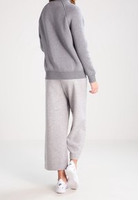 Felpa grigia con colletto e polsini a coste, abbinata a pantaloni da tuta larghi grigi chiari. Scarpe da ginnastica bianche completano l'outfit.