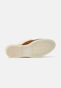 Scarpa slip-on in suede marrone con fodera morbida color crema, suola in gomma con motivi circolari per la presa e marchio impresso sulla suola.