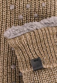 Bruin gebreid stof met verhoogde grijze stippen, een zachte grijze fleecelaag aan de binnenzijde en een zwart leren label aan de onderkant.