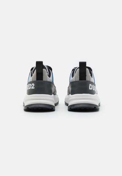 Vista posteriore di sneakers che presentano una parte superiore grigia e nera, dettagli blu, intersuola bianca e suola nera con un motivo di trazione visibile.