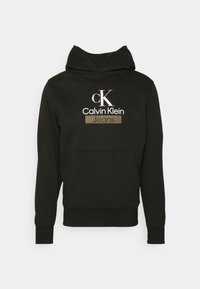 Felpa nera con tasca frontale, dotata di un logo "Calvin Klein Jeans" bianco e oro. Tessuto morbido e polsini a coste.