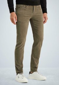 Maslinasto zelene slim-fit traperice s pet džepova, šivaćim detaljima i glatkom mješavinom pamuka. Uparene su s bijelim niskim tenisicama.