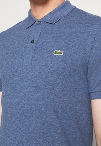Pique polo-shirt i mörkblått, med klassisk krage, två knappar och en grön broderad krokodil-logga på vänster bröst.