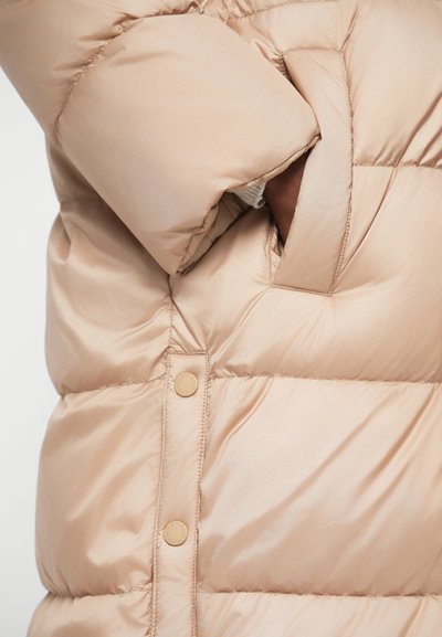 Beige színű pufi dzseki állítós dizájnnal, sima textúrával, oldalzsebbel és patentgombokkal az alján.