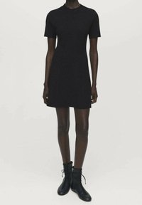 Robe noire à manches courtes avec un col rond, une coupe ajustée, un tissu texturé et une finition lisse, associée à des bottines noires à lacets.