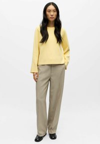 Kollane pikavarrukaga topp, ümar lõige, koos beežide kohandatud pükste ja mustade kingadega, valge taustaga.