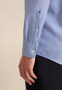 Camicia blu a motivo con piccoli punti blu su uno sfondo azzurro chiaro, con polsini con bottoni e un design aderente.