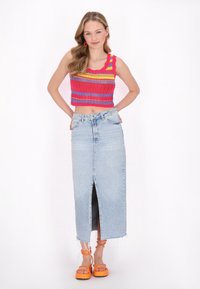 Pletený crop top v červených, růžových a žlutých pruzích, spárovaný se světle modrou denimovou sukní s předním rozparkem a třepeným lemem. Oranžové platformové sandály.