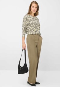 Lichtgewicht, bedrukt bovenstuk met driekwart mouwen in beige, zwart en groen; hoge taille, op maat gemaakte olijfgroene broek; zwarte schoudertas.