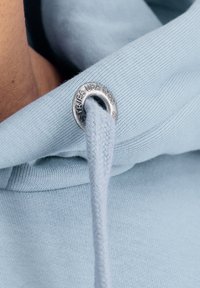 Svijetloplavi dukserica s tkanom vezicom i srebrnim metalnim rupama. Glatka tekstura tkanine s rebrastim manžetama i rubom.