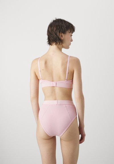 Lyserød ribbet bralette med justerbare stropper og hægclosure, parret med højtaljede matchende trusser med blød tekstur og sømløst design.