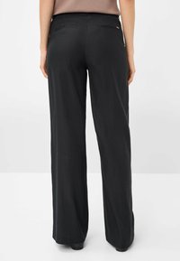 Pantaloni neri a gamba larga caratterizzati da una texture liscia, un leggero luccichio e due tasche posteriori dal design elegante. L'orlo si ferma poco sopra le scarpe.