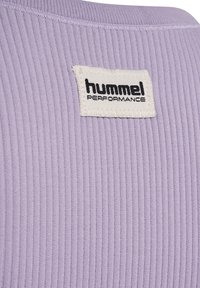 Gros plan d’un tissu côtelé lavande avec une étiquette rectangulaire blanche portant la mention "hummel PERFORMANCE" en lettres noires.