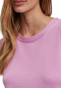 Kurzärmliges pinkes Strickoberteil mit rundem Ausschnitt, das eine glatte Textur und ein nahtloses Design aufweist, teilweise im oberen Brustbereich sichtbar.