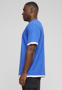 T-shirt bleu à manches courtes en coton avec des poignets rayés blancs contrastants. Ourlet droit, coupe décontractée, texture lisse et détails minimaux.