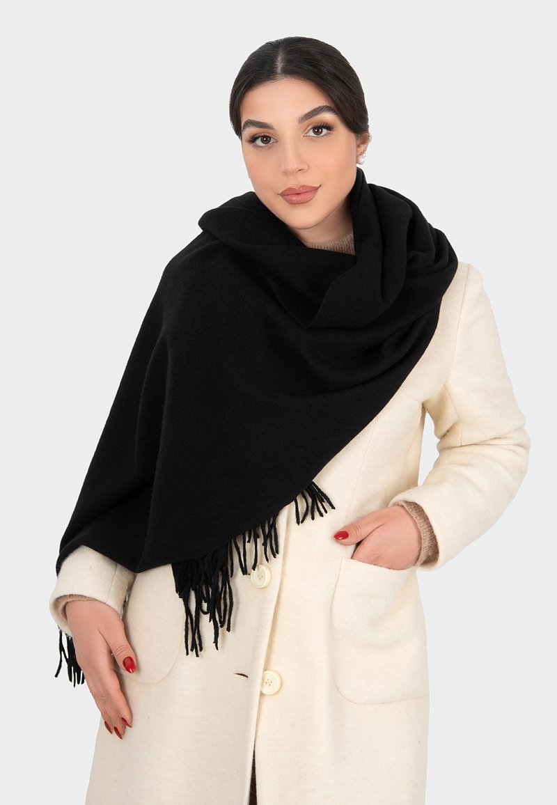 Sciarpa nera con bordi frangiati, realizzata in tessuto morbido, adagiata su un cappotto color crema. Texture liscia, design versatile e misura generosa.