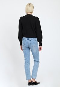 Schwarzer, strukturierter Pullover mit Puffärmeln; kombiniert mit hellblauen, enganliegenden Jeans. Schwarze Schuhe teilweise sichtbar. Einfaches, schlichtes Design.