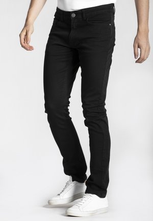 Jean slim noir en tissu durable, doté de cinq poches, d'une fermeture à bouton en métal et d'un détail de couture ton sur ton. Associé à des baskets blanches.