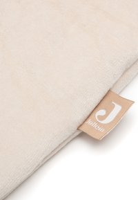 Gros plan sur un tissu beige doux avec une petite étiquette beige affichant une lettre blanche "J" et le nom de la marque "Jollein".