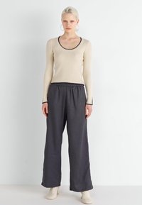 Top beige a righe a maniche lunghe con scollatura rotonda, abbinato a pantaloni larghi grigio scuro con vita elastica. Stivali col tacco neutri.