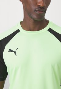 Limonaadiroheline spordisärk mustade võrkpinkidega varruka- ja õlavarreaktsentidega. Vasakul rinnal on must Puma logo.