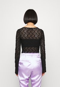 Black lace long-sleeve top with floral pattern, cropped style. Paired with high-waisted lavender satin pants, smooth texture.