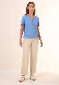 Top azzurro chiaro a maniche corte con scollatura a V e una texture sottile, abbinato a pantaloni beige a gamba larga e sneakers bianche con dettagli blu.