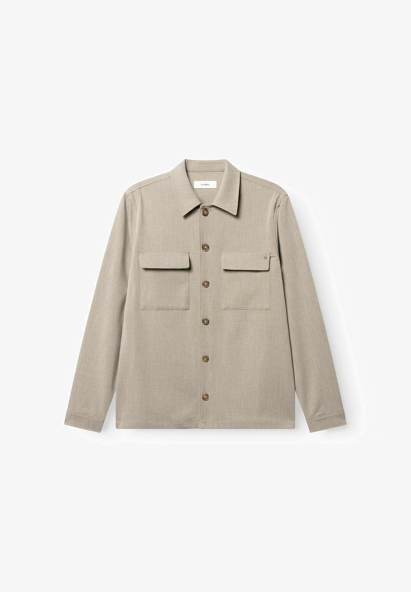 Chemise beige à manches longues avec boutons, deux poches à rabat sur la poitrine et un col pointu sur fond blanc.